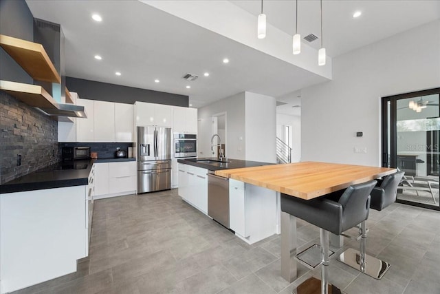 kitchen with decorative light fixtures, an island with sink, sink, white cabinets, and stainless steel appliances