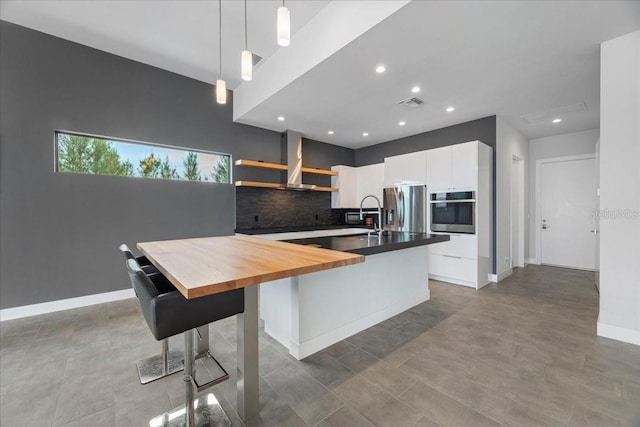 kitchen featuring tasteful backsplash, decorative light fixtures, white cabinets, stainless steel appliances, and wall chimney range hood