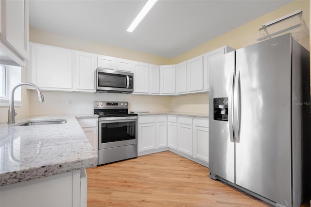 kitchen featuring light stone countertops, light wood-type flooring, stainless steel appliances, sink, and white cabinets