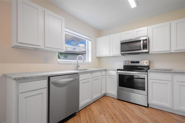 kitchen featuring stainless steel appliances, white cabinetry, light hardwood / wood-style floors, and sink