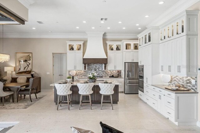 kitchen featuring a breakfast bar area, premium range hood, a kitchen island with sink, stainless steel appliances, and white cabinetry