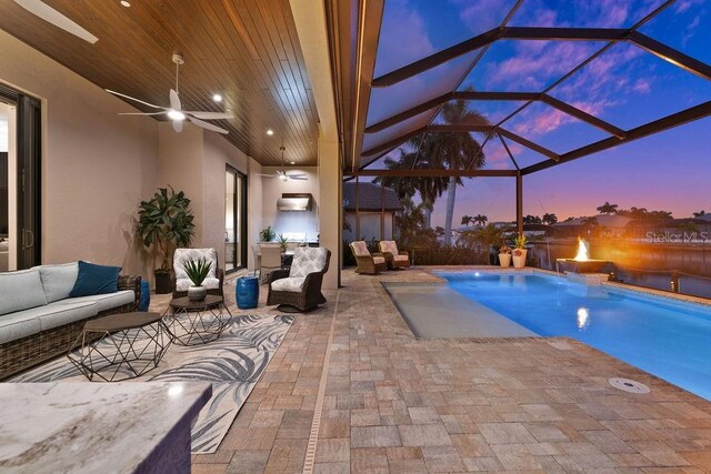 pool at dusk featuring an outdoor living space, a lanai, pool water feature, ceiling fan, and a patio