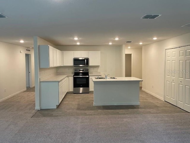 kitchen with dark carpet, a kitchen island with sink, sink, white cabinets, and appliances with stainless steel finishes