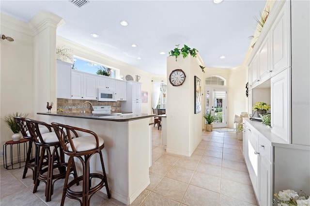 kitchen with kitchen peninsula, backsplash, ornamental molding, white appliances, and white cabinets