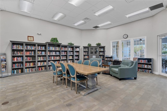 carpeted dining space featuring a drop ceiling and a towering ceiling