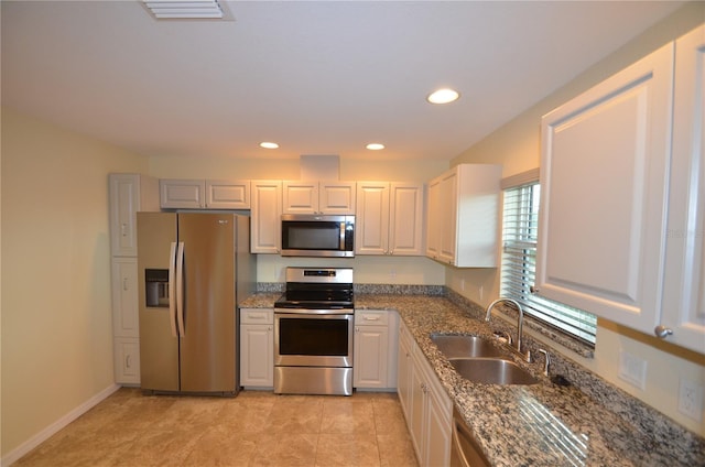 kitchen with appliances with stainless steel finishes, white cabinets, stone countertops, light tile patterned floors, and sink