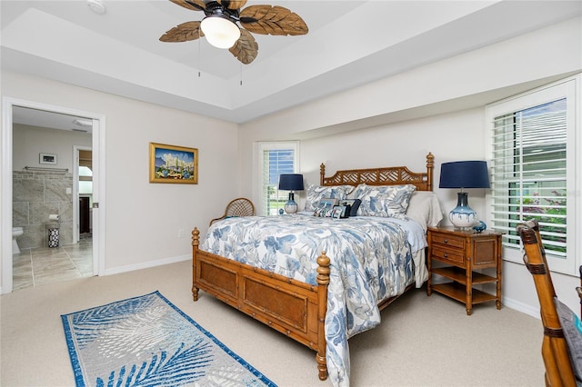 carpeted bedroom featuring multiple windows, a tray ceiling, ensuite bath, and ceiling fan