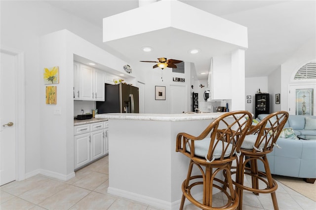 kitchen with white cabinets, kitchen peninsula, light tile patterned floors, ceiling fan, and stainless steel fridge