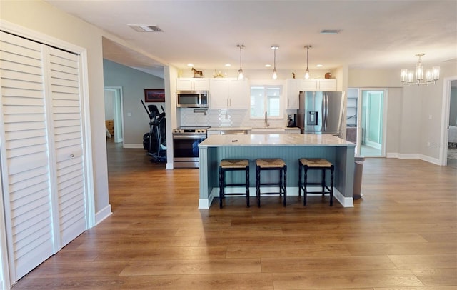 kitchen with white cabinets, appliances with stainless steel finishes, wood-type flooring, pendant lighting, and a kitchen island