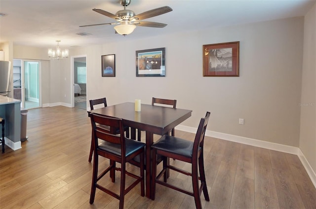 dining room with ceiling fan with notable chandelier and light hardwood / wood-style floors