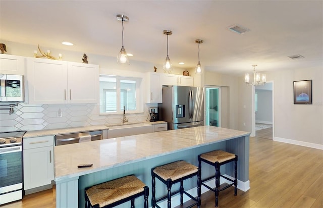 kitchen with white cabinets, a center island, light wood-type flooring, stainless steel appliances, and sink