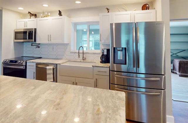 kitchen featuring stainless steel appliances, sink, light stone countertops, and white cabinets