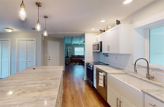 kitchen with white cabinetry, light hardwood / wood-style flooring, light stone counters, hanging light fixtures, and appliances with stainless steel finishes