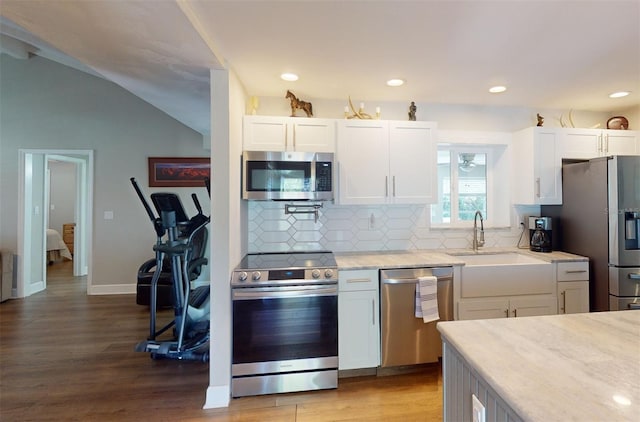 kitchen with white cabinets, stainless steel appliances, lofted ceiling, wood-type flooring, and decorative backsplash