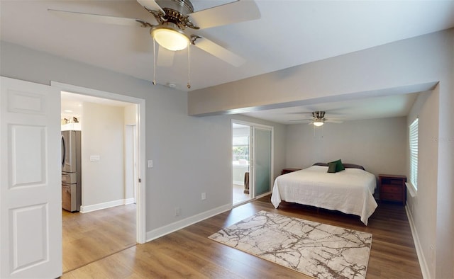 bedroom featuring connected bathroom, hardwood / wood-style floors, stainless steel refrigerator, and ceiling fan