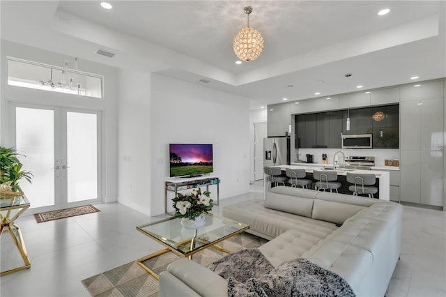 living room featuring french doors, a tray ceiling, and sink