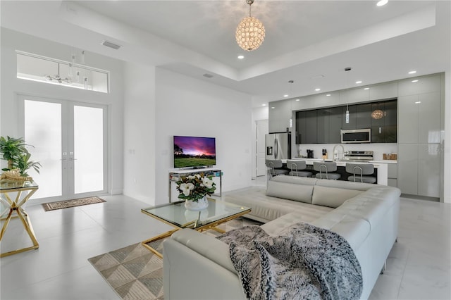 living room featuring sink, french doors, a raised ceiling, and a high ceiling