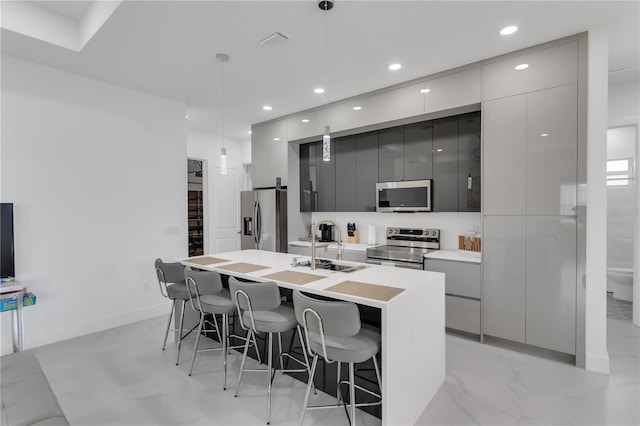 kitchen featuring sink, a breakfast bar area, appliances with stainless steel finishes, a kitchen island with sink, and hanging light fixtures