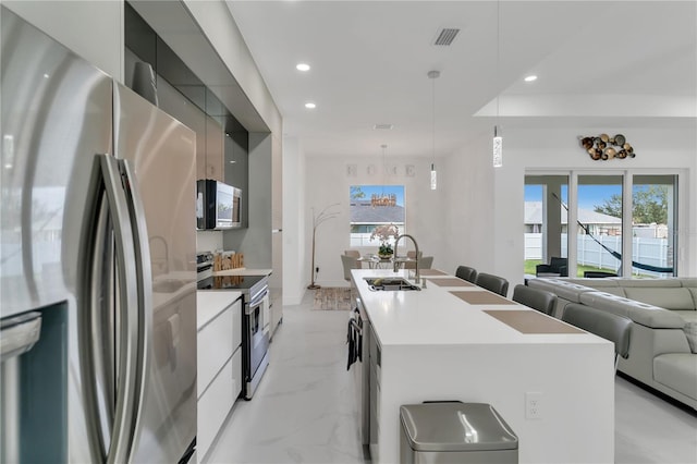 kitchen with sink, appliances with stainless steel finishes, hanging light fixtures, an island with sink, and a healthy amount of sunlight