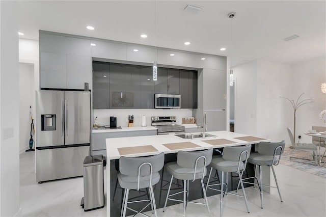 kitchen featuring gray cabinetry, hanging light fixtures, stainless steel appliances, and a breakfast bar