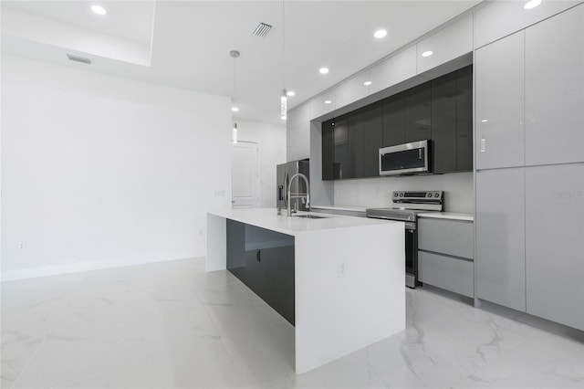 kitchen featuring a kitchen island with sink, hanging light fixtures, sink, and appliances with stainless steel finishes