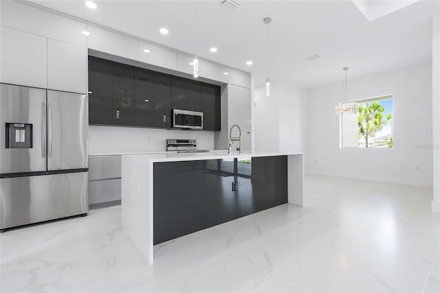 kitchen featuring sink, white cabinetry, pendant lighting, stainless steel appliances, and a kitchen island with sink