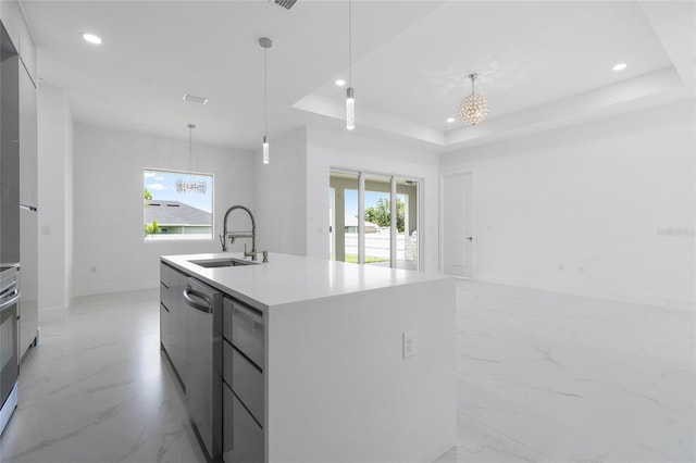 kitchen with a raised ceiling, a kitchen island with sink, sink, and decorative light fixtures