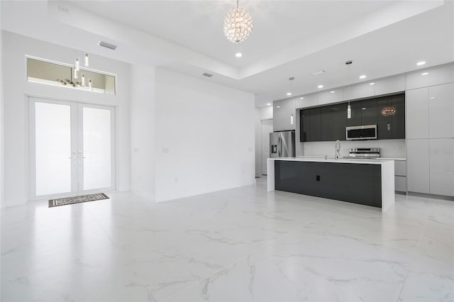 kitchen with pendant lighting, appliances with stainless steel finishes, an inviting chandelier, a center island with sink, and french doors