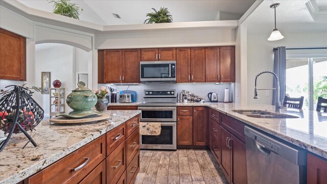 kitchen with light hardwood / wood-style floors, stainless steel appliances, sink, backsplash, and pendant lighting