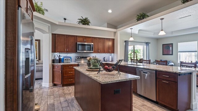 kitchen with light hardwood / wood-style floors, decorative light fixtures, appliances with stainless steel finishes, and a center island