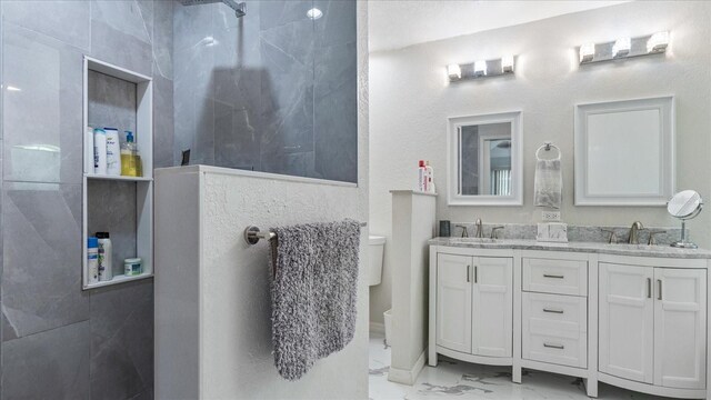 bathroom featuring a tile shower, vanity, and toilet