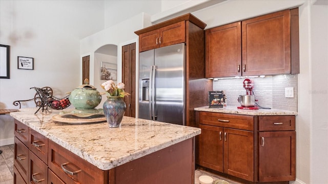 kitchen with built in refrigerator, light tile patterned floors, light stone countertops, decorative backsplash, and a center island