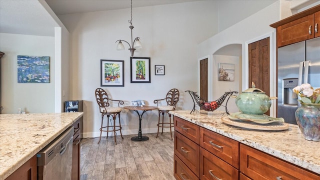 kitchen with appliances with stainless steel finishes, light stone counters, light hardwood / wood-style floors, and decorative light fixtures