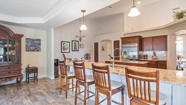 kitchen with stainless steel built in fridge, light hardwood / wood-style floors, hanging light fixtures, crown molding, and light stone countertops