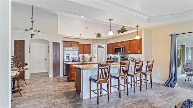 kitchen featuring light wood-type flooring, stainless steel appliances, light stone counters, and decorative light fixtures