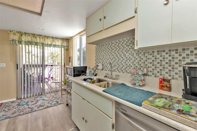 kitchen featuring light hardwood / wood-style floors, white cabinetry, backsplash, stainless steel dishwasher, and sink