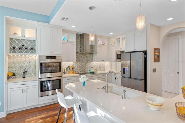 kitchen with wall chimney exhaust hood, light wood-type flooring, appliances with stainless steel finishes, and decorative light fixtures