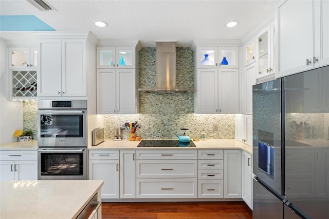 kitchen featuring stainless steel appliances, white cabinets, and wall chimney range hood