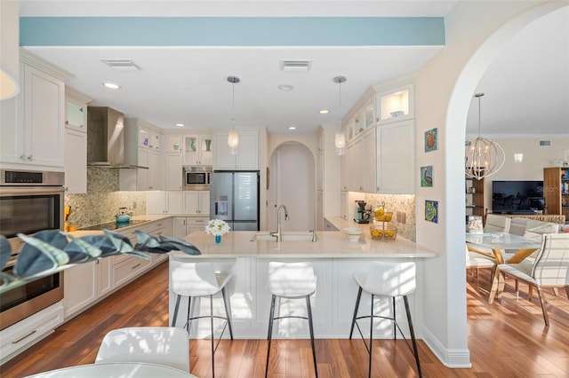 kitchen with hanging light fixtures, sink, wall chimney exhaust hood, hardwood / wood-style flooring, and stainless steel appliances