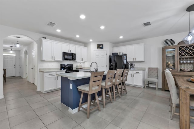 kitchen featuring an island with sink, white cabinets, a kitchen bar, black appliances, and decorative light fixtures