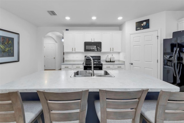 kitchen featuring an island with sink, sink, white cabinetry, and black appliances