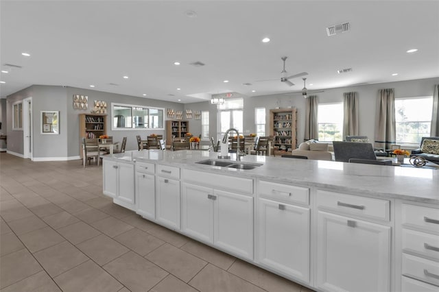 kitchen with light stone counters, white cabinets, light tile patterned floors, ceiling fan, and sink