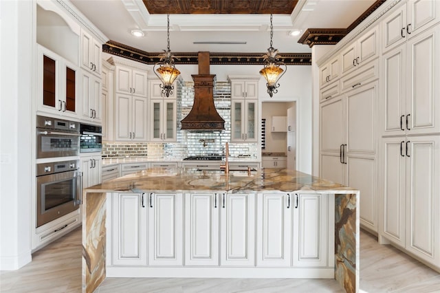 kitchen featuring light stone counters, pendant lighting, an island with sink, and a raised ceiling