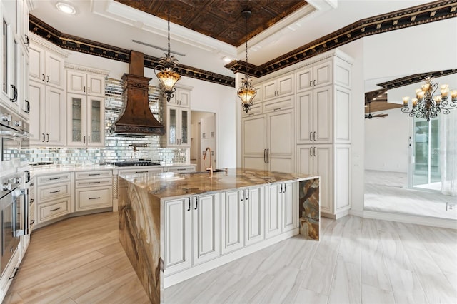 kitchen featuring tasteful backsplash, a kitchen island with sink, pendant lighting, custom exhaust hood, and ornamental molding