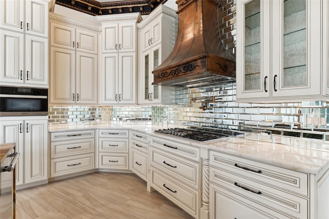 kitchen featuring decorative backsplash, stainless steel appliances, light stone countertops, and custom exhaust hood