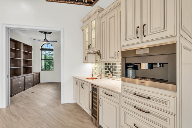 kitchen featuring ceiling fan, light stone counters, cream cabinets, beverage cooler, and decorative backsplash