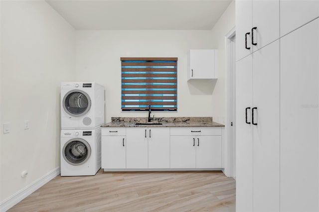 clothes washing area featuring cabinets, light wood-type flooring, sink, and stacked washer / drying machine