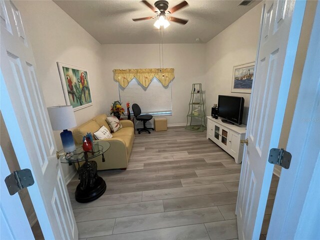 living room featuring ceiling fan, a textured ceiling, and light hardwood / wood-style flooring