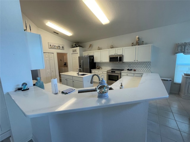 kitchen featuring light tile patterned flooring, white cabinets, vaulted ceiling, kitchen peninsula, and appliances with stainless steel finishes