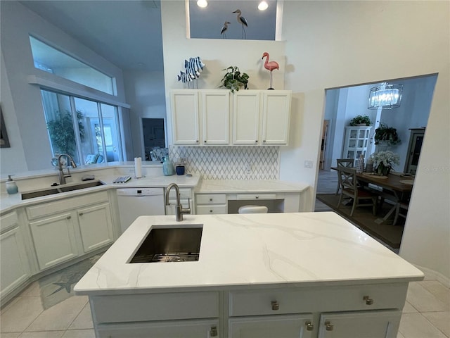 kitchen with dishwasher, sink, an inviting chandelier, a center island with sink, and light stone countertops